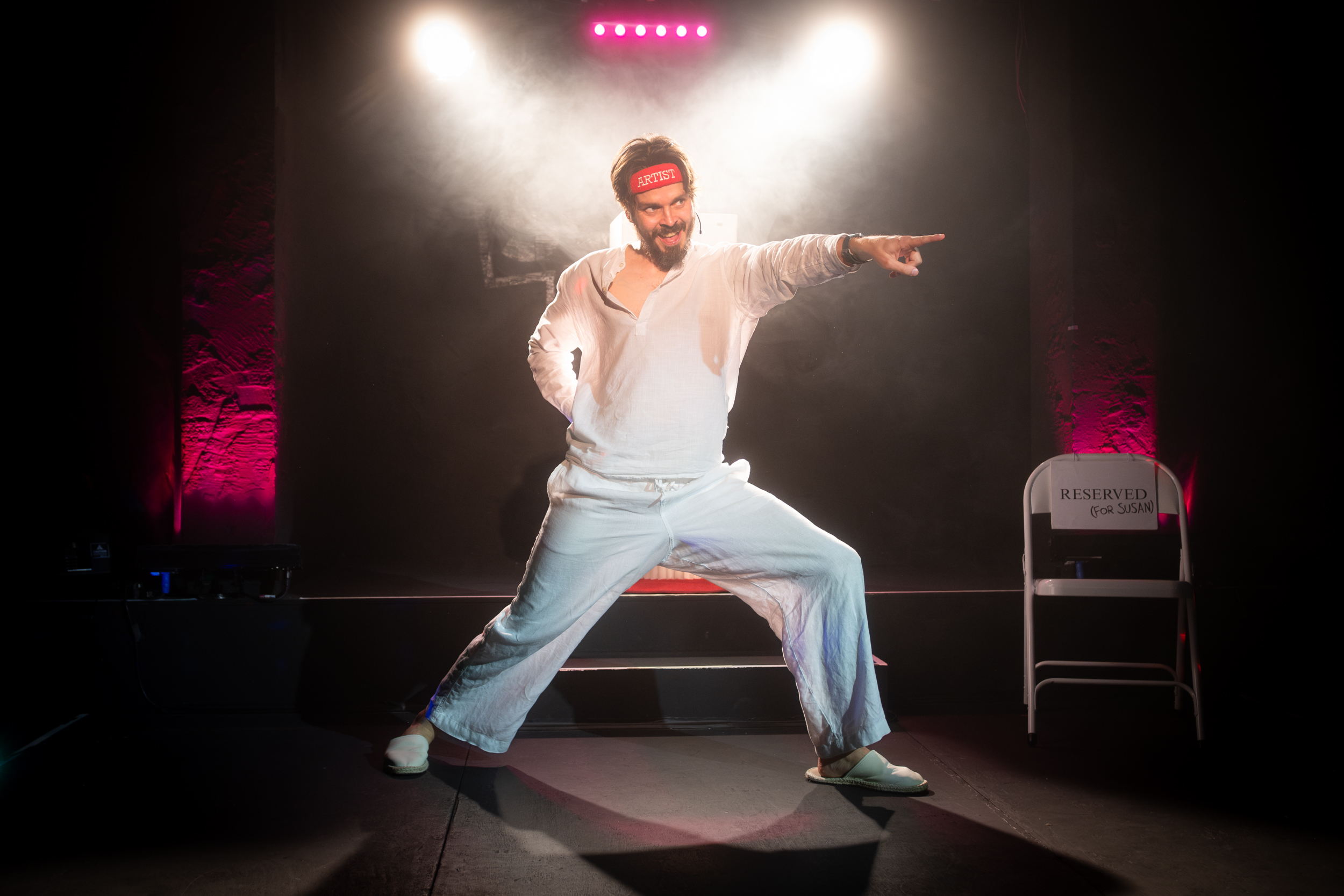 Joz Norris on stage in a lunge and pointing at the audience.