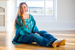 A woman in blue shirt and jeans sat on wood floor.