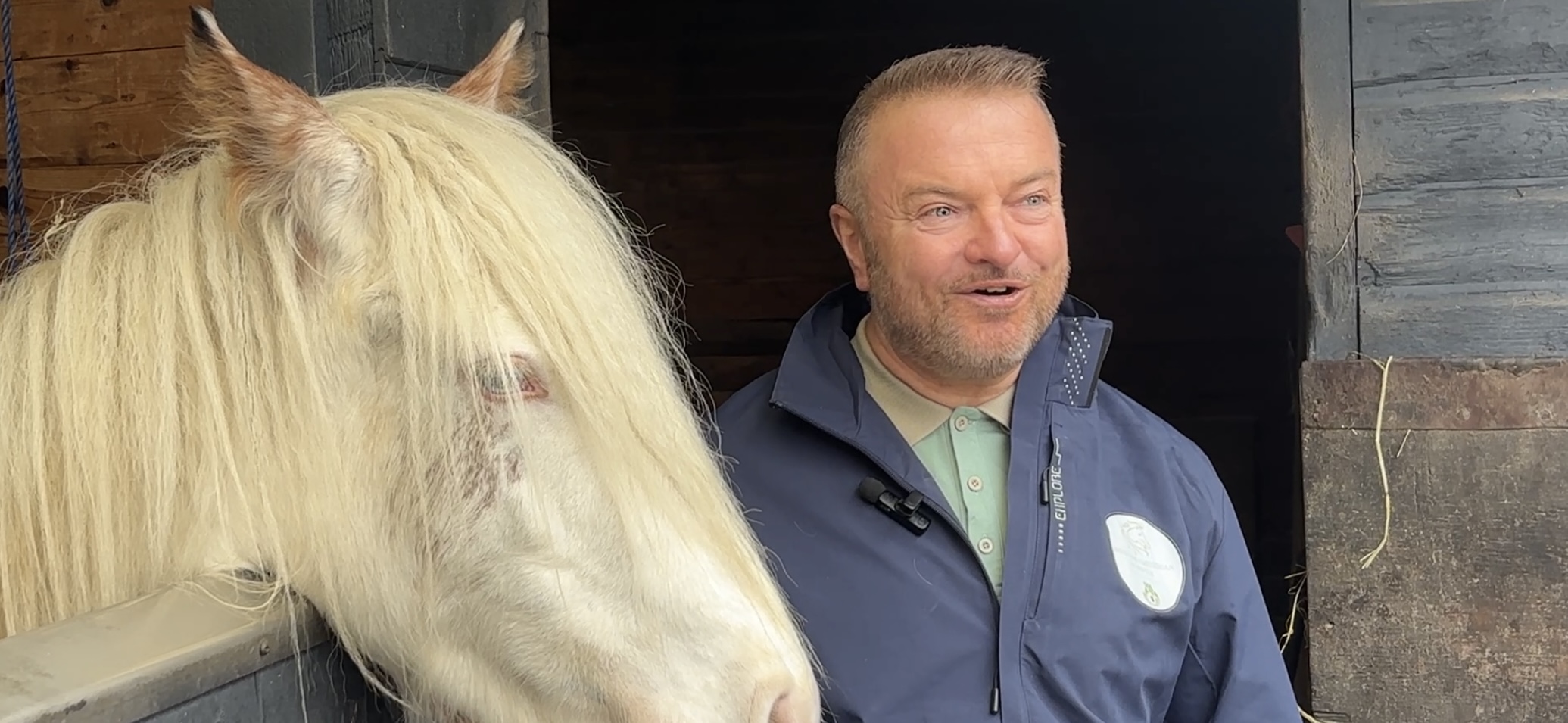 White horse to the left of the image with a middle aged man to the right of the image.